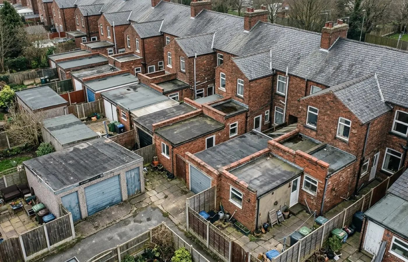 A row of flat-roofed rear extensions and garages behind older housing, felt and single-ply coverings meeting brick upstands